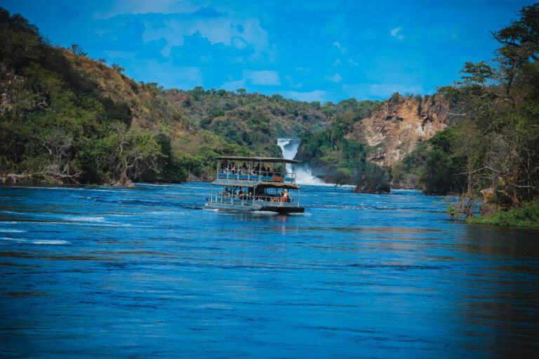 A tourist boat cruising the Victoria Nile in Murchison Falls National Park, Uganda, with spray from the falls in the distance.